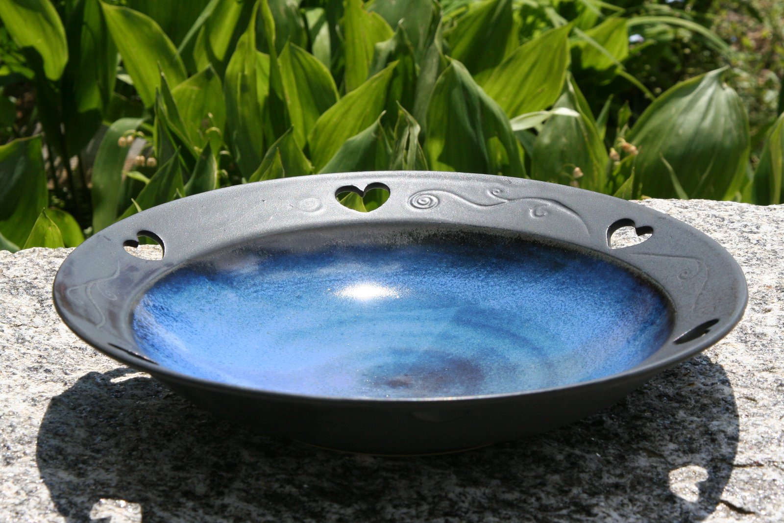 Handgetöpferte Schale mit blauer Glasur und herzförmigen Aussparungen im Garten